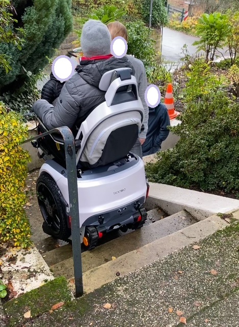 Ich fahre mit dem Scewo Bro Elektrorollstuhl Treppen hoch. Um mich herum stehen drei Mitarbeiter der Firma und des Sanitätshauses und leiten mich an.