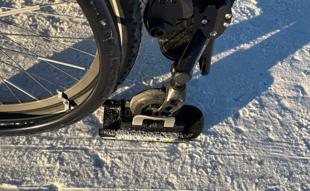 Ein Rollstuhl im Schnee mit Wheel Blade Skiern unter den kleinen Vorderrädern des Rollstuhls.